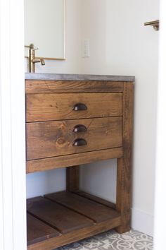 a wooden cabinet with two drawers and a mirror on the wall in a white room