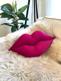 a large pink pillow on top of a white chair next to a potted plant