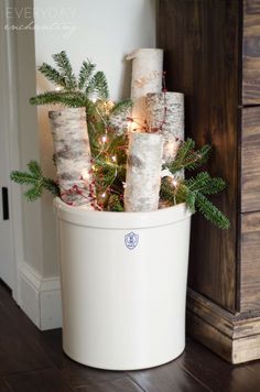 a christmas tree in a white bucket with lights on the top and some branches sticking out of it