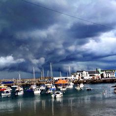 many boats are docked in the water under a cloudy sky