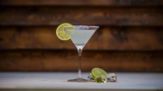 a martini glass with limes on the rim and an ice cube next to it