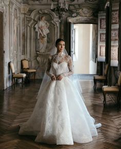 a woman in a wedding dress standing on a wooden floor next to a chandelier