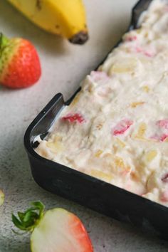 a pan filled with fruit and ice cream next to some strawberries on the table