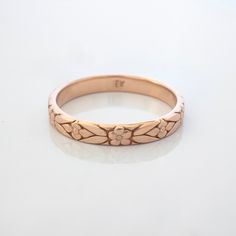 a rose gold wedding ring on a white background with reflection in the middle and small flower design at the top