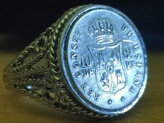 a silver ring with a crown on it sitting on top of a wooden table next to a coin