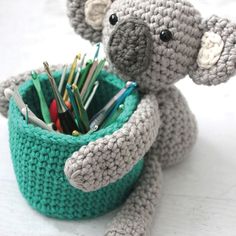 a crocheted teddy bear sitting in a cup with pens and pencils inside