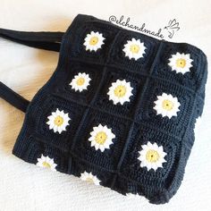 a crocheted black purse with white and yellow flowers on the front, sitting on a bed