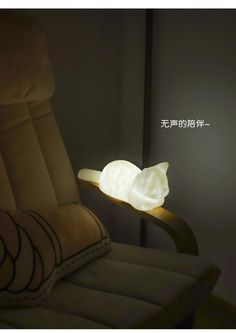 a cat lamp sitting on top of a chair next to a pillow in the dark