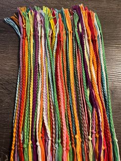 several rows of multicolored braids laid out on a wooden table, with one string in the middle