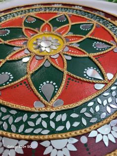 an ornately decorated table top with gold and red designs on the edges, sitting on a green surface