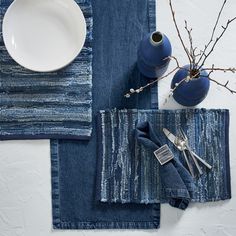 a place setting with blue linens and silverware on the table, next to a vase