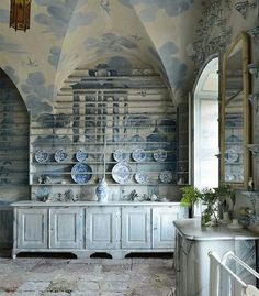 an ornately decorated room with blue and white plates on the wall, vases and shelves