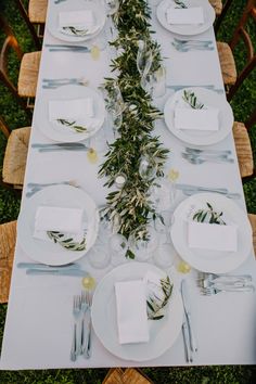 the table is set with white plates and silverware, napkins and greenery