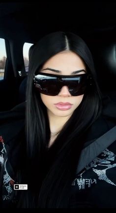 a woman with long black hair and sunglasses in the back seat of a car looking at the camera