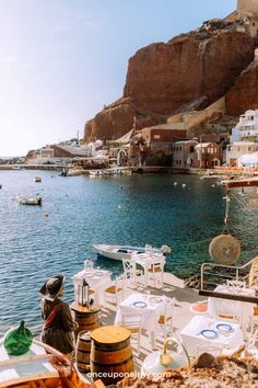 an outdoor dining area overlooking the water with boats in the harbor and houses on the cliff side