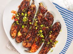 a white plate topped with grilled eggplant covered in sauce and green onions