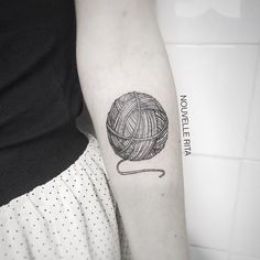 a ball of yarn is on the arm of a woman with a black and white tattoo