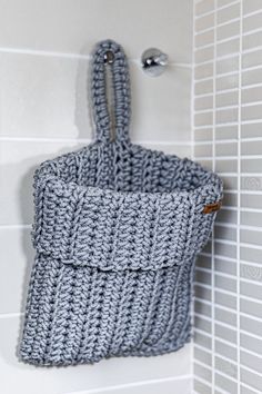 a gray crocheted bag hanging on the wall next to a white tiled shower