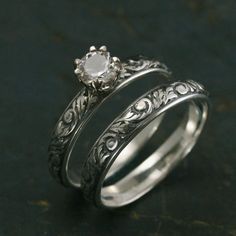 two wedding rings with an engraved design on each side and a diamond in the middle