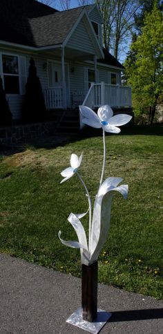 a metal flower sculpture sitting on top of a wooden block in front of a house