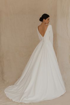 a woman in a white wedding dress standing against a wall with her back turned to the camera