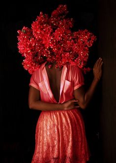 a woman with red flowers on her head standing in front of a dark background, wearing a pink dress