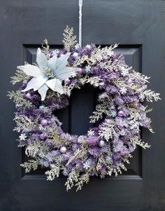 a wreath with purple and silver decorations hanging on a black front door, surrounded by snowflakes