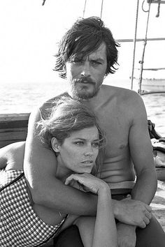 a man and woman sitting on top of a bench next to each other in front of the ocean