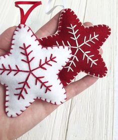 a hand holding two red and white felt snowflake ornament hanging from a string