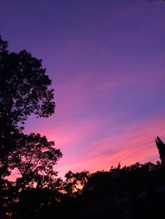 the sun is setting behind some trees in the distance, with purple and pink clouds