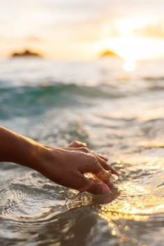 a person's hand reaching for something in the water on a sunny day at the beach