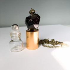 a small bottle with a necklace on it sitting next to a chain and glass bottle