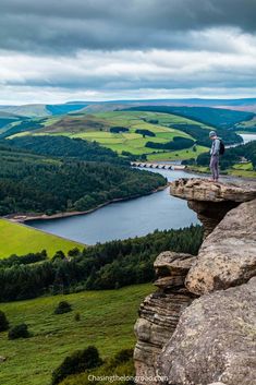 a man standing on top of a cliff next to a body of water in the distance