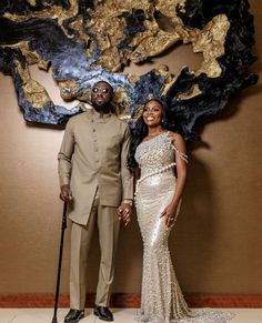 a man and woman standing next to each other in front of a wall with art