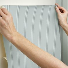 a woman is holding up a lamp shade to the wall with her hands on it