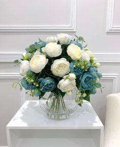 a vase filled with white and blue flowers sitting on top of a table next to a chair