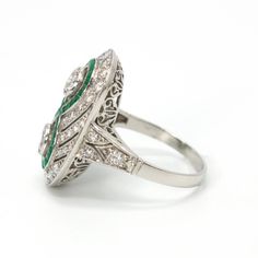 This jaw dropping ring, an Art Deco piece of art likely made in the 1920s, is made of platinum and features two central bezel set diamonds ensconced by an infinity-style figure eight channel of square cut emeralds. The rest of the ring's top contains multiple angular swirls of diamonds that are separated by pierced cut-outs, giving a palpable sense of motion to the piece. The shoulders are beautifully pierced and the undercarriage—or gallery—is ornately filigreed. Metal: Platinum Main Stones: 2 Round Brilliant Diamonds (approx. 0.66 carat total, G color, SI1-SI2 clarity, natural, 4.4 mm) Accent Stones: 42 Round Brilliant Diamonds (approx. 0.82 carat total, F-H color, VS1-SI2 clarity, natural, 1.0 - 2.3 mm) & 40 Square Cut Emeralds (approx. 0.40 carat total, natural) Ring Size: 7.25 (can be Nature Ring, Bezel Set Diamond, Art Deco Diamond, Square Cut, Brilliant Diamond, Bezel Setting, Cut Outs, Round Brilliant, Precious Metals