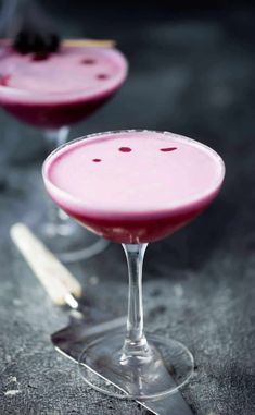 two glasses filled with pink drinks sitting on top of a gray countertop next to each other