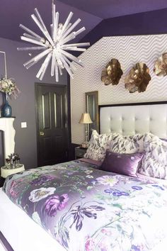 a bedroom with purple and white bedding, chandelier and mirror on the wall