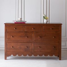 a wooden dresser with two vases on top of it next to a white wall