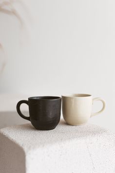 two black and white coffee cups sitting on top of a cement block next to each other