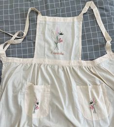 an apron with embroidered flowers on it sitting on top of a bed next to a pillow