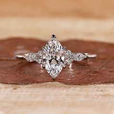 an oval cut diamond engagement ring on top of a wooden surface with leaves in the foreground