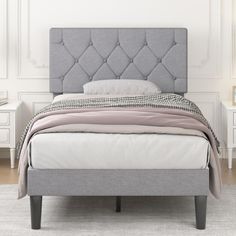 a bed with a gray upholstered headboard and foot board in a white room