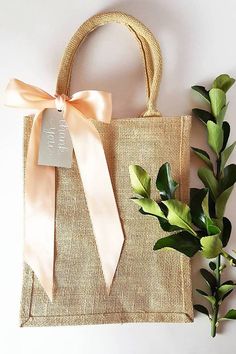 a bag with a ribbon tied around it next to a plant and some leaves on the table