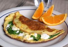 an omelet with spinach, cheese and orange slices on a white plate