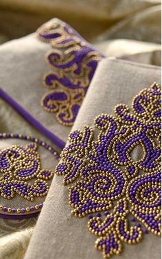 two purple and gold embroidered napkins sitting on top of each other, one with beading