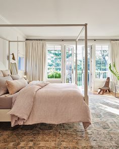 a bedroom with a four poster bed and beige linens on the pillows, along with an area rug