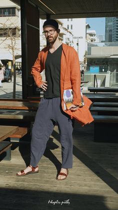 a man in an orange jacket and hat standing on a wooden platform with his hands in his pockets