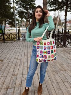 a woman is holding a multicolored bag on her shoulder and posing for the camera